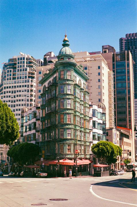 A green and white ornate building with a domed roof stands at a street corner in a city.