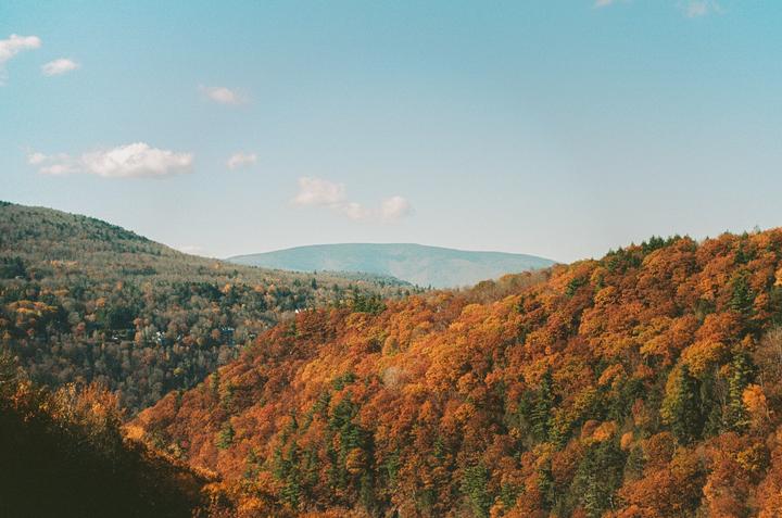 A landscape view shows mountains covered in autumn foliage under a clear sky with a few clouds.