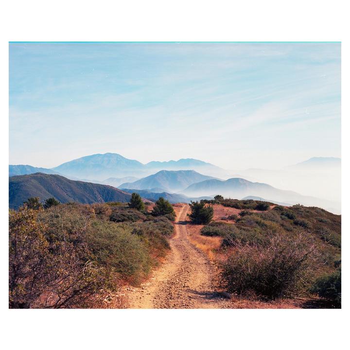A dirt road winds through a mountainous landscape with hazy blue peaks in the distance.