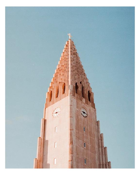 A tall, light-colored church tower with a cross on top stands against a clear blue sky.