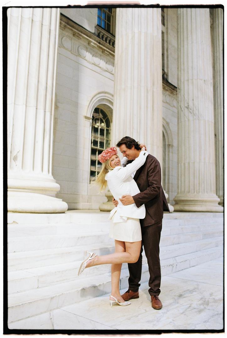 A couple embraces on the steps of a building with large columns.