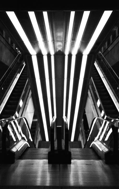 A symmetrical view of escalators and bright overhead lights in a metro station.