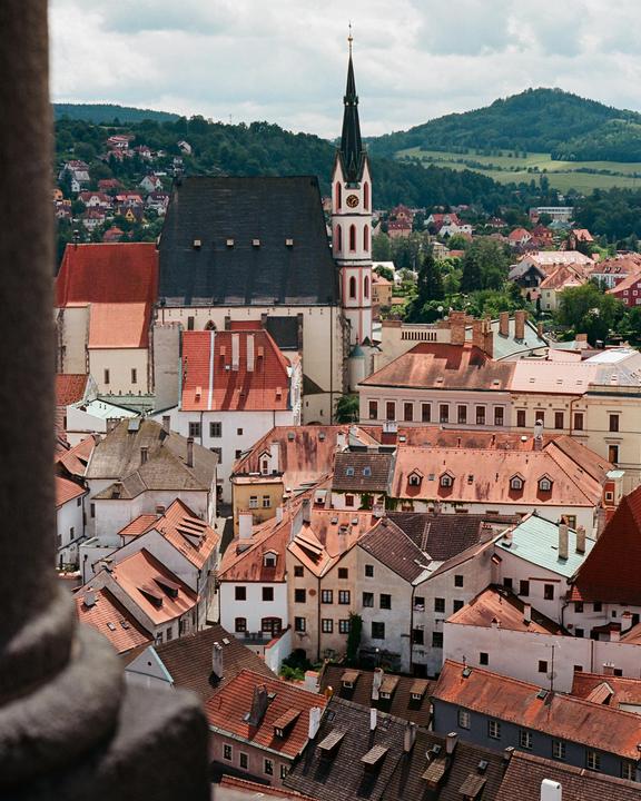 A high-angle view shows the red roofs of a town with a tall church steeple and green hills in the background.