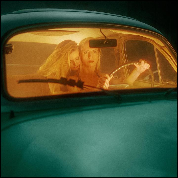 Two women are visible through the windshield of a car at night.
