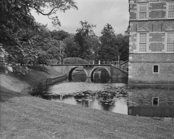 A brick castle with many windows stands next to a moat with a bridge over it.