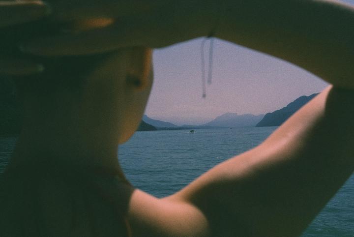 A person's arms frame a view of a lake with mountains in the distance.