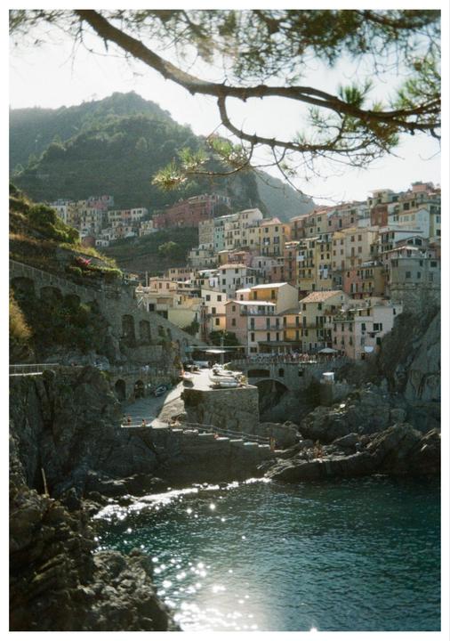 A coastal town with colorful buildings is nestled into a hillside above a sparkling body of water.