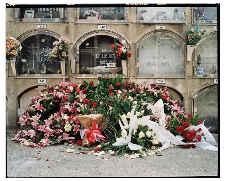 A wall of crypts with glass doors is adorned with numerous bouquets of flowers and ribbons.