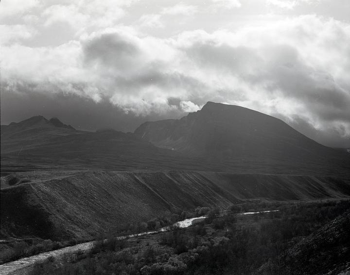 A river flows through a valley with mountains under a cloudy sky.