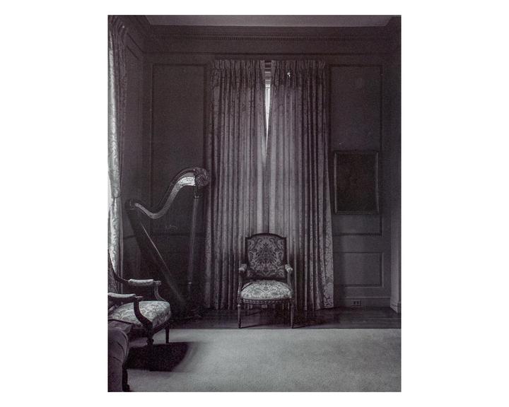A harp and two ornate chairs are arranged in a dimly lit room with heavy curtains.