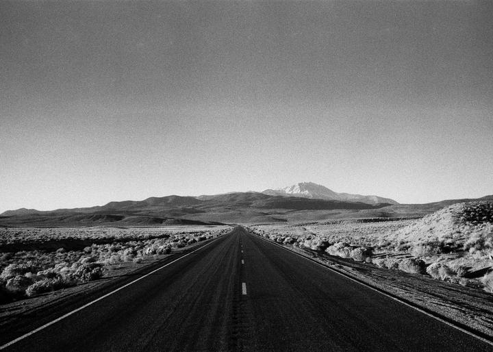 A long, straight road extends into the distance through a desert landscape with mountains under a clear sky.