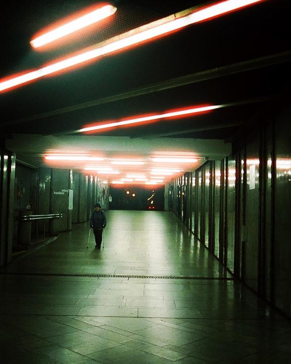A person with a cane walks down a long, brightly lit underground passageway.