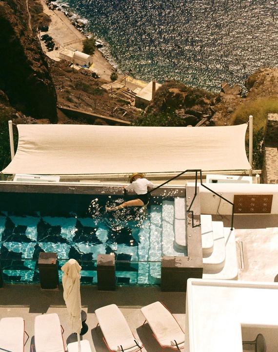 A woman in a straw hat is sitting in a swimming pool overlooking the sea.