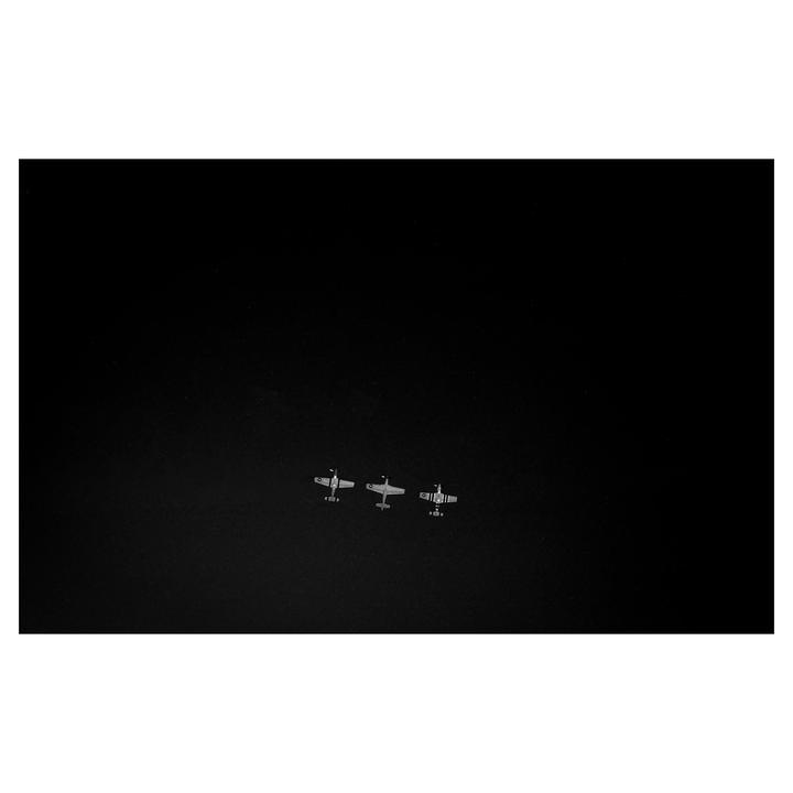 Three small airplanes fly in formation against a dark sky.