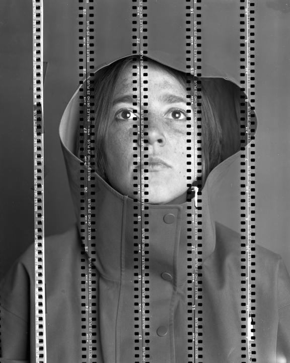 A woman wearing a hooded jacket looks directly forward, with strips of film laid over her face.