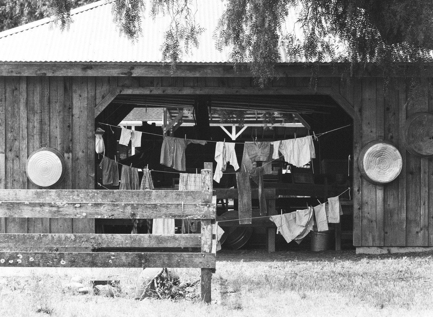 Laundry hangs on a clothesline in front of a wooden barn with a metal roof.