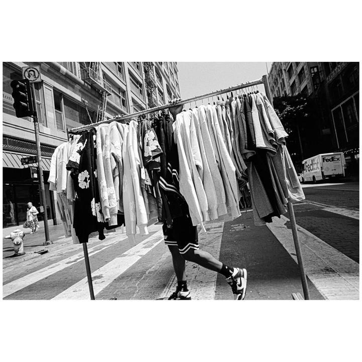 A person walks on a street carrying a clothing rack full of garments.