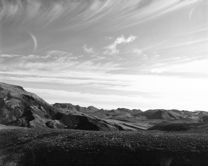 A vast, rugged landscape with mountains and a textured foreground stretches under a sky with wispy clouds.