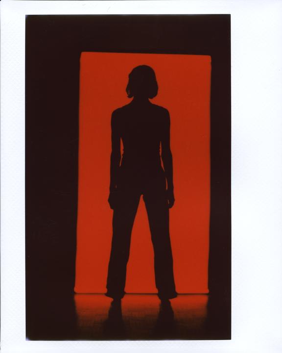 A silhouette of a woman stands against a bright red background.