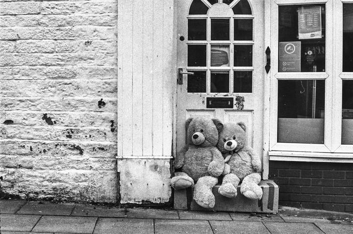 Two teddy bears sit on a step in front of a door and window.
