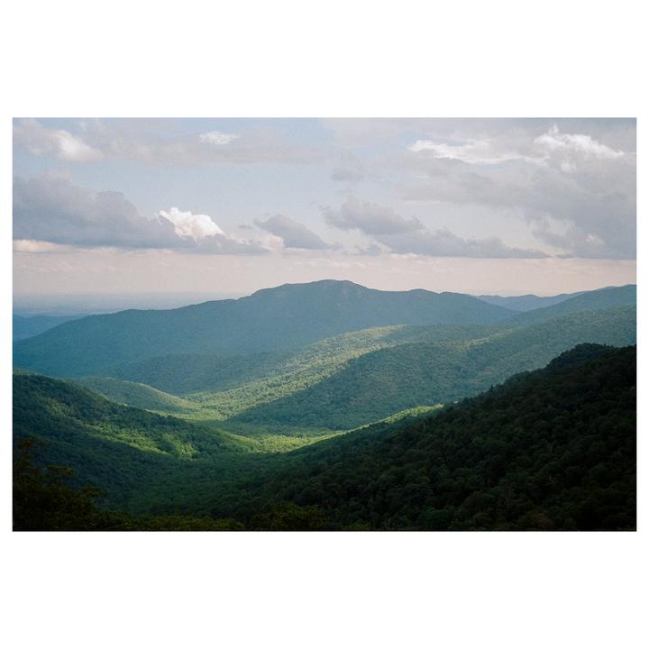 A valley of green mountains is visible under a cloudy sky.