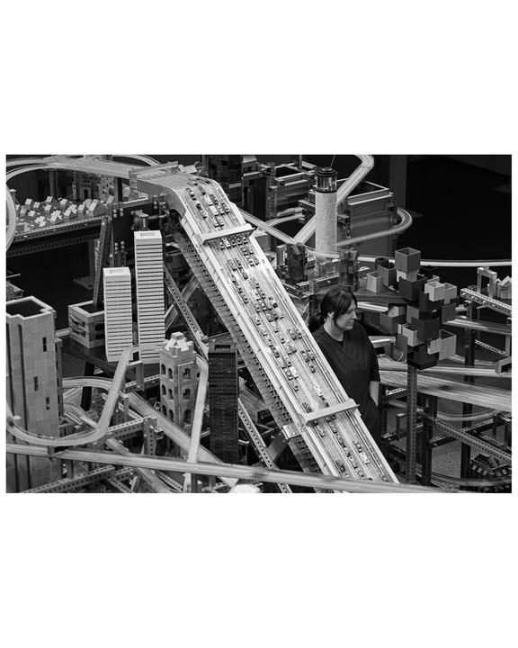 A woman stands next to a large, intricate model of a city with many roads and buildings.