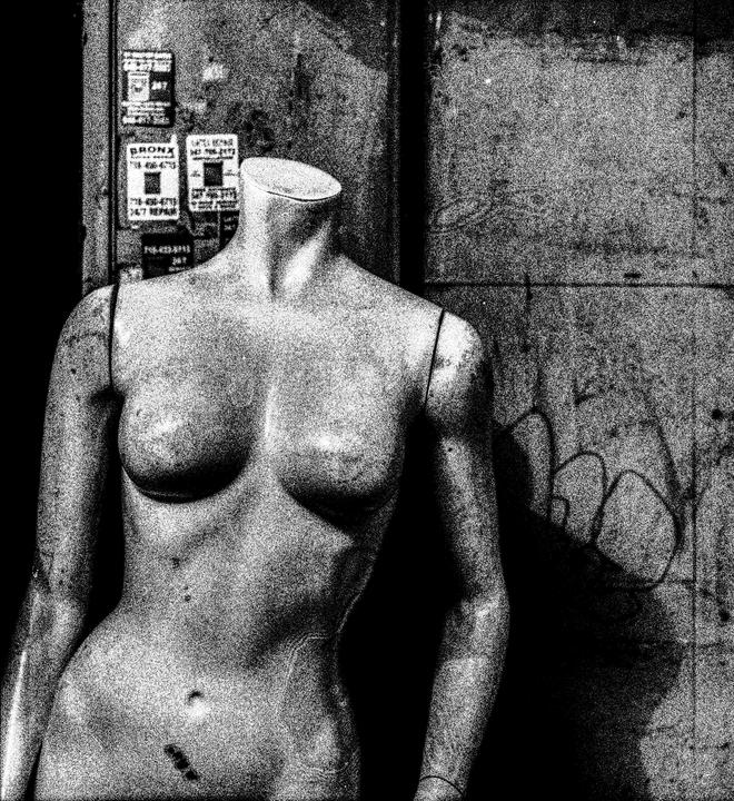 A headless mannequin stands in front of a wall with graffiti and posters.