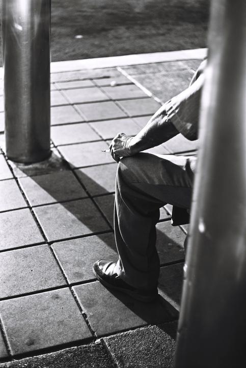 A person sits on a tiled surface, holding a cigarette between their fingers.