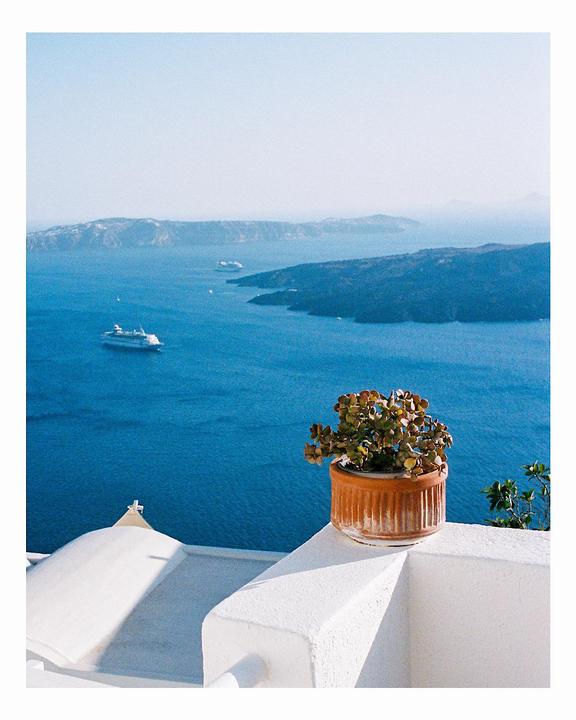 A potted plant sits on a white wall overlooking a bay with islands and boats.