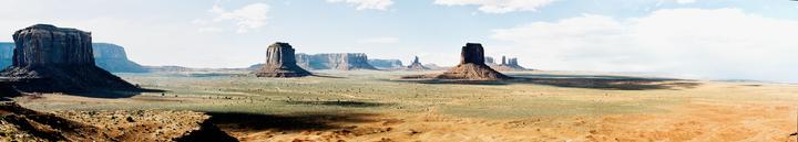 A panoramic landscape shows several large rock formations in a desert under a partly cloudy sky.