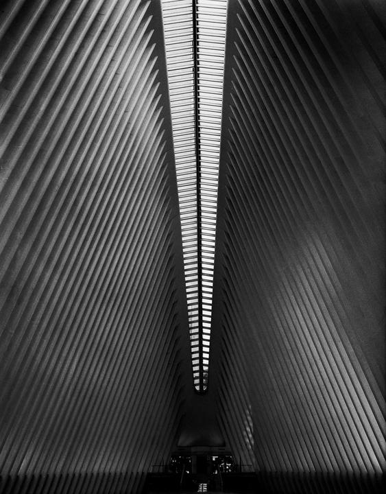A long, narrow skylight runs down the center of a tall, ribbed, modern building interior.