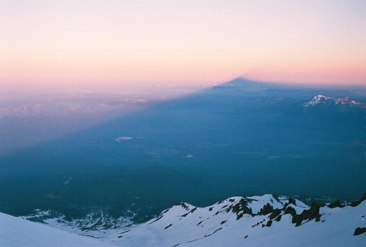 A mountain casts a long shadow over a valley at sunrise.