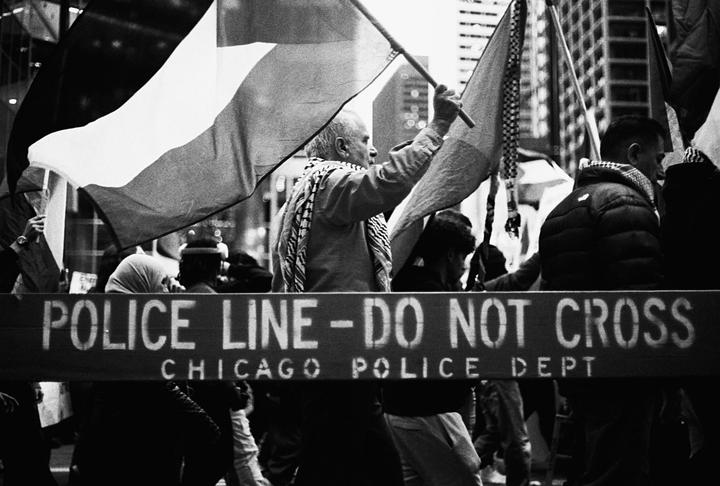 A man holds a flag behind a "Police Line - Do Not Cross" barrier in Chicago.