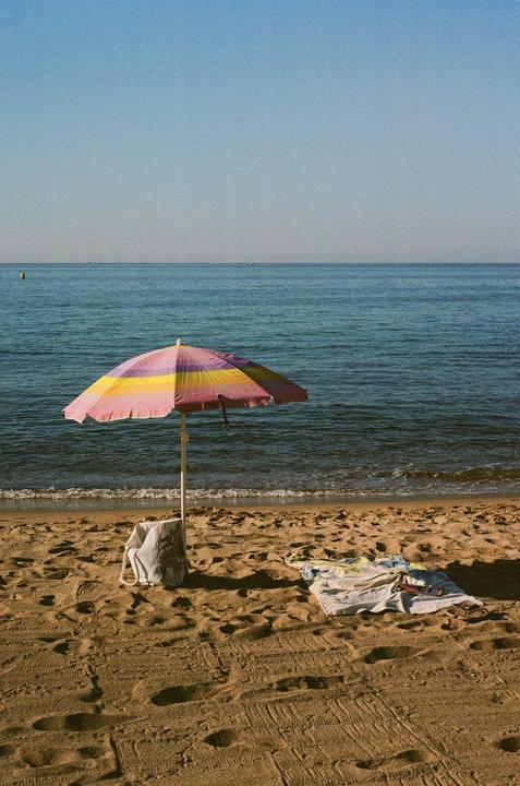 A colorful beach umbrella stands on a sandy beach next to the ocean.