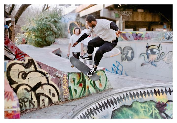 A man on a skateboard performs a trick in a graffiti-covered skatepark.