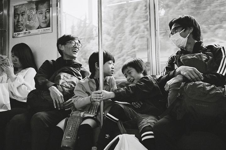 People are sitting on a train, with one man laughing and two children interacting.