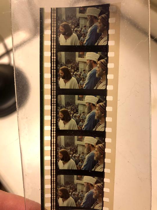 A strip of film shows a man with long hair and a beard in a crowd of people.