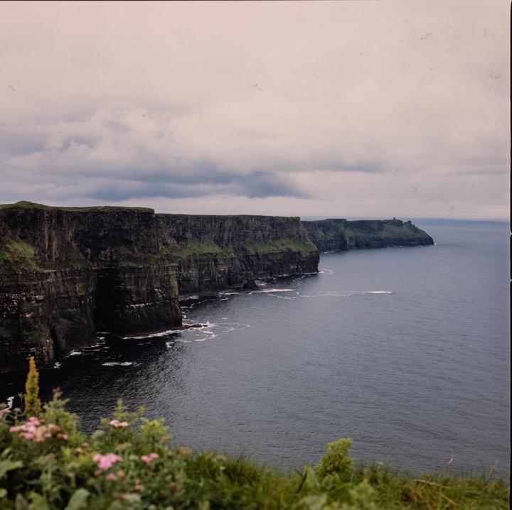 A dramatic view of the Cliffs of Moher shows the rugged coastline meeting the ocean under a cloudy sky.