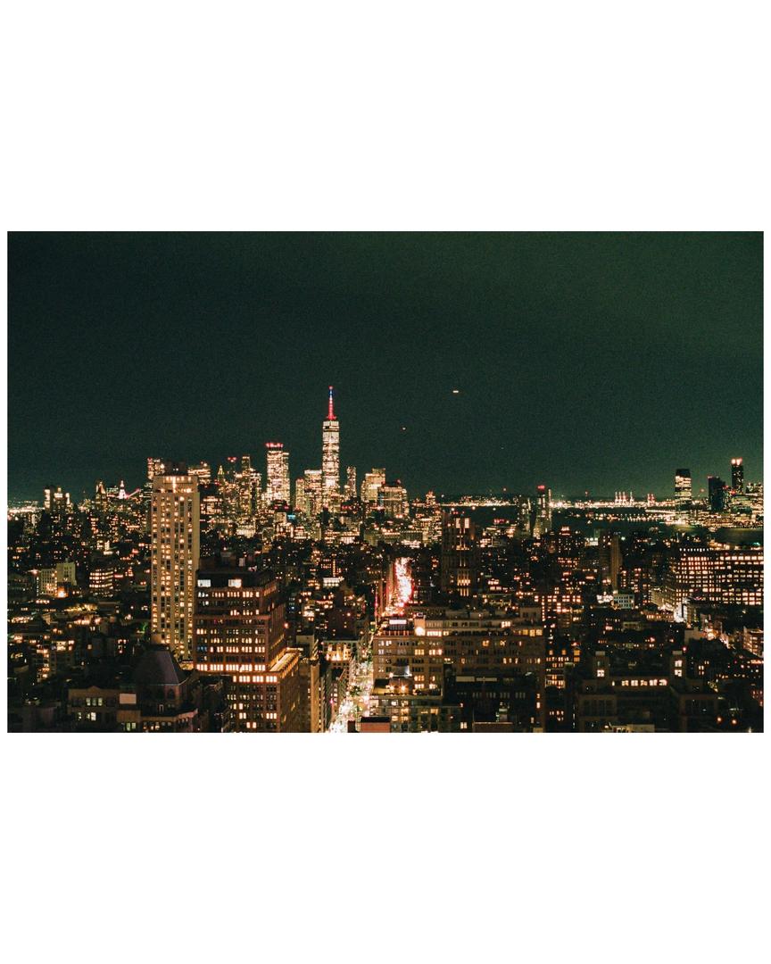 A city skyline is illuminated at night with a prominent skyscraper in the distance.