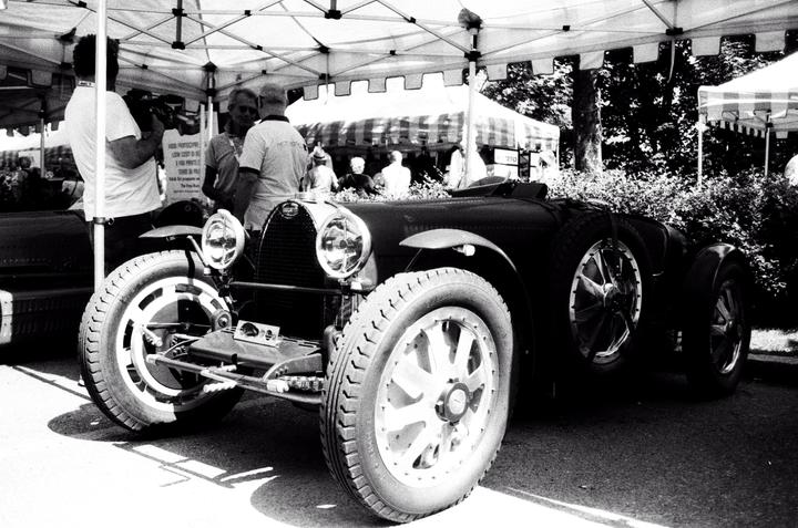 A vintage Bugatti Type 35 car is parked under a tent with people standing around it.