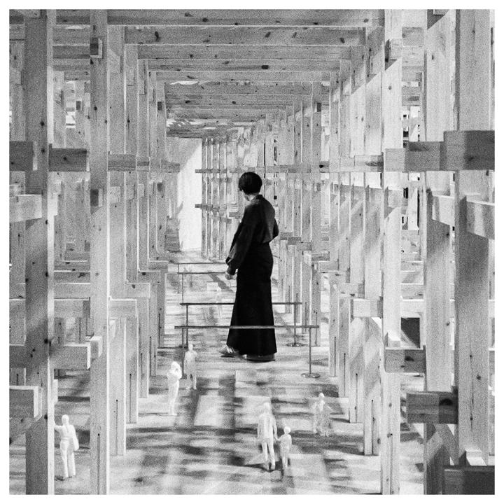 A woman stands in a room constructed from many wooden beams, looking down at small figures on the floor.