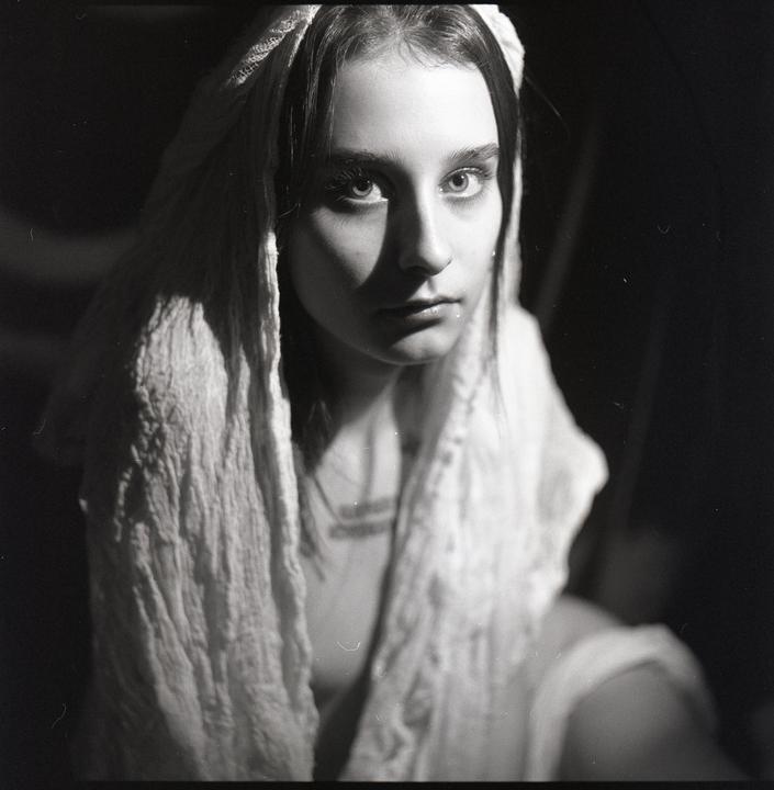 A woman with a white head covering looks directly at the viewer.
