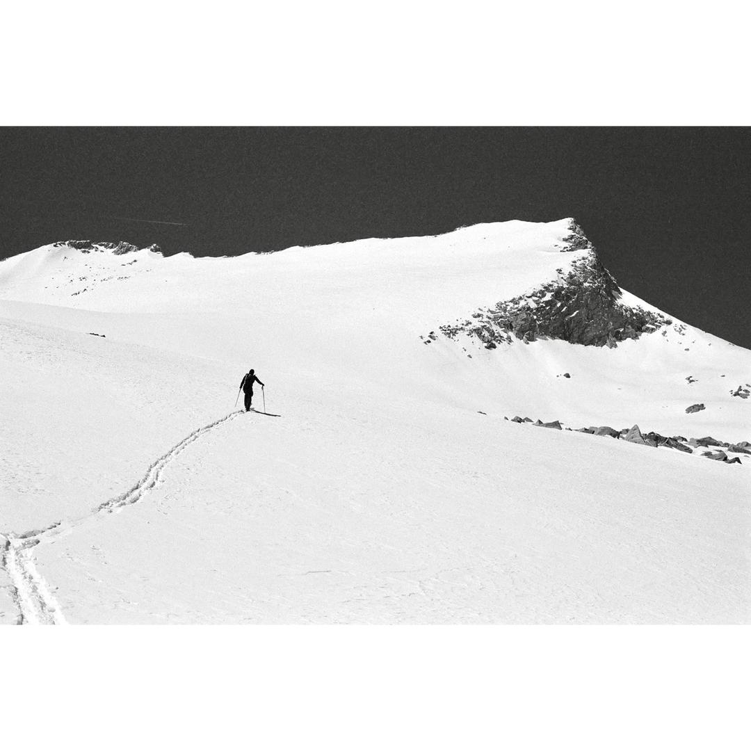A person skis across a snow-covered mountain with a dark sky above.