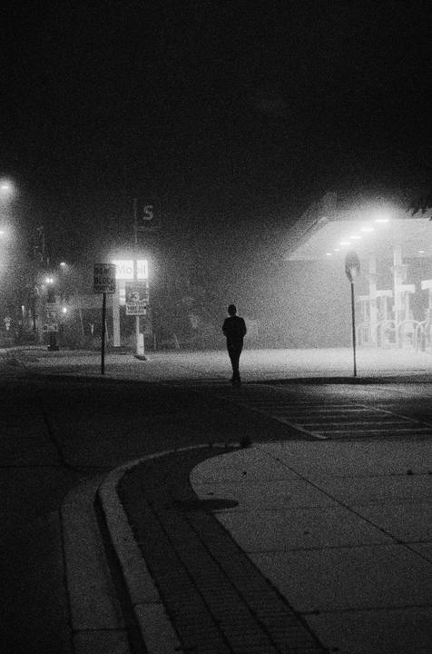 A person walks towards a brightly lit gas station at night.