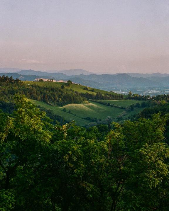 A vast landscape of rolling green hills and distant mountains is seen under a pale sky.
