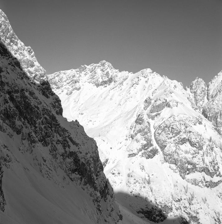 A black and white landscape shows snow-covered mountains under a clear sky.