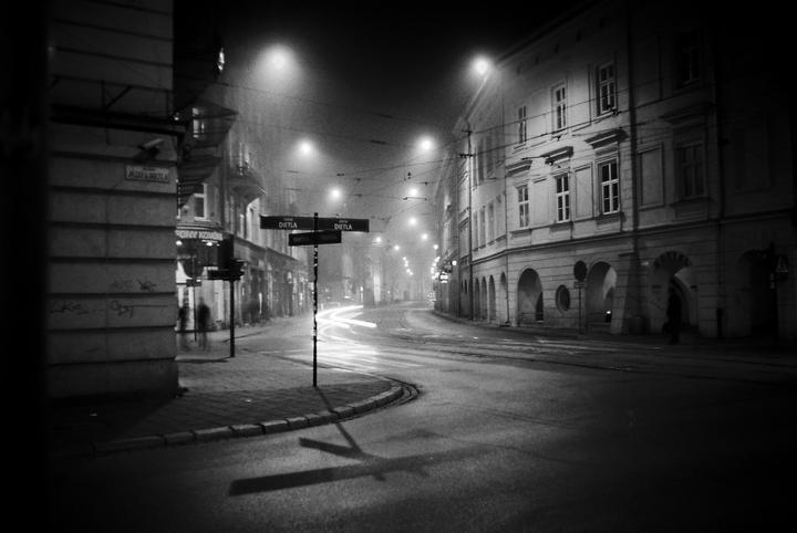 A street sign for Dietla street stands at a corner with light trails from vehicles on a foggy night.