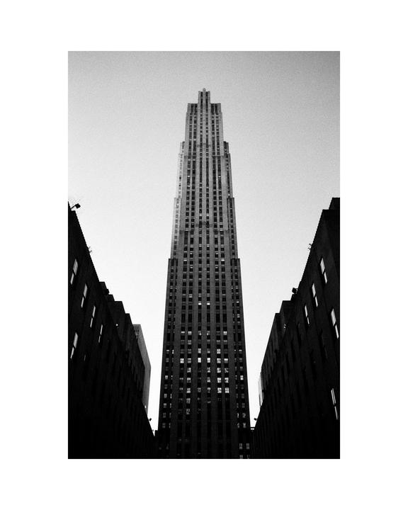 A tall skyscraper stands between two dark buildings, viewed from below.