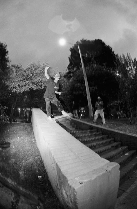 A skateboarder grinds a ledge at night with a full moon and trees in the background.