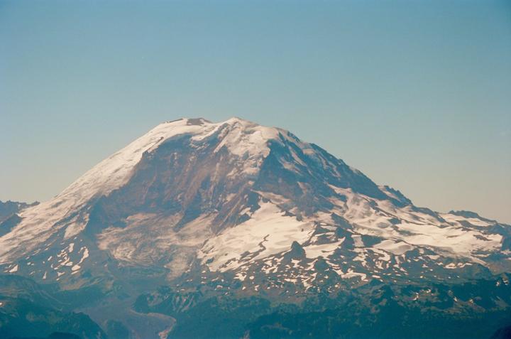 A snow-capped mountain rises majestically against a clear sky, with green foothills visible below.